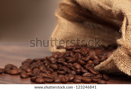 Coffee beans in coffee bag made from burlap on wooden surface with dramatic light. Focused on foreground.