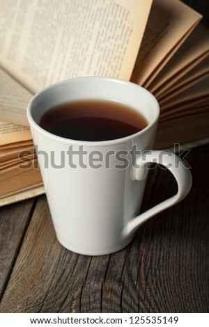 Cup of tea with old opened book on wooden table. Focused on cup.