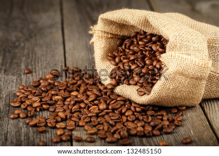 Coffee beans in coffee bag made from burlap on wooden surface. Focused in middle of the frame.