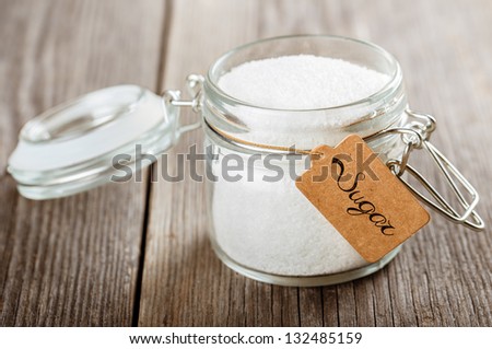 Opened glass jar with sugar. Standing on wooden table