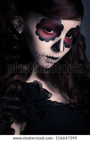 Low key portrait of young woman with sugar skull make-up.