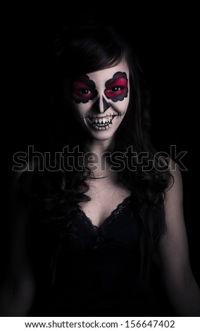 Low key portrait of smiling young woman with sugar skull make-up.