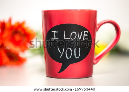 Red ceramic cup with I love you sign made with chalk. Standing on a kitchen table.