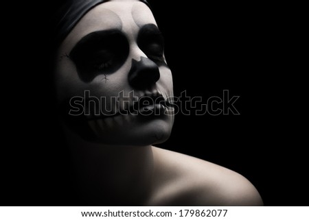 Low key portrait of young woman with skull make-up.
