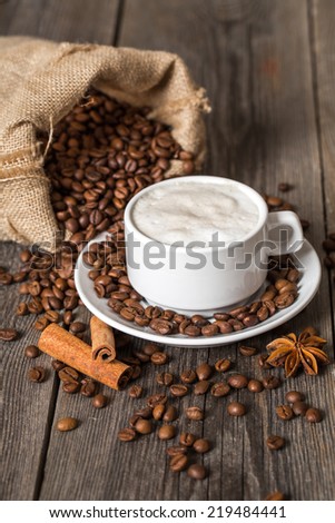 Coffee cup with cinnamon sticks and coffee bag on wooden table