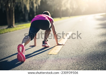 Sportive woman working out outdoors. Young lady doing exercises and ready to start running. Health and sport concept.
