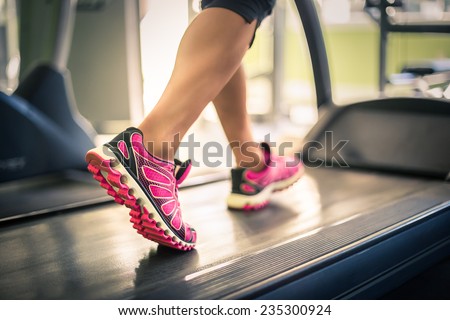 Fitness girl running on treadmill. Woman with muscular legs in gym