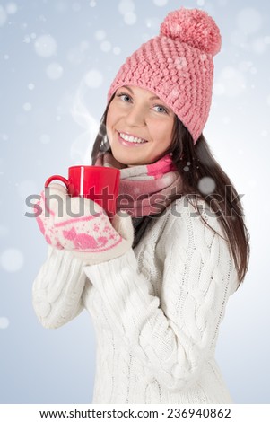 Smiley young woman in winter outfit with red cup. With snowflakes background.