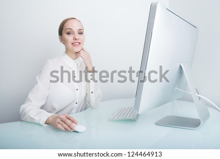 Attractive smiling young business woman working on computer in the office at the desk looking at the camera