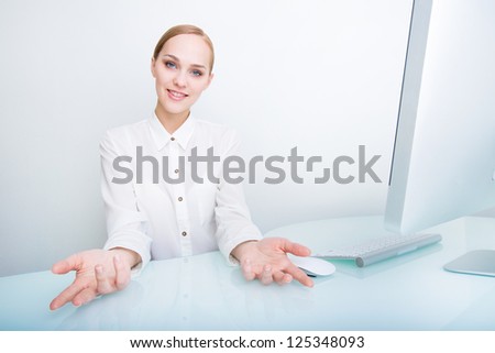 Portrait of a happy young business woman shows her open hands in welcome gesture over the office