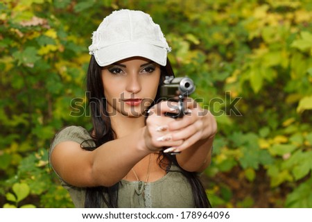 Beautiful young girl in a cap with a gun in his hands. Outdoors.