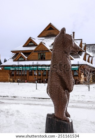 Wooden figure of bear and rural hotel in winter ski resort