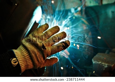 Hand in worker glove shadowing welding sparks