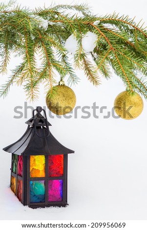 Multicolored decorative lantern in the snow and fur-tree branch with golden Christmas balls