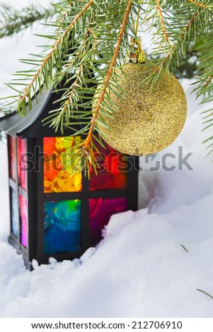 Multicolored decorative lantern in the snow and fur-tree branch with golden Christmas ball