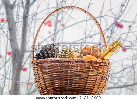 Christmas basket with fruits, nuts and champagne at the window on the background of the trees with red apples on a rainy day