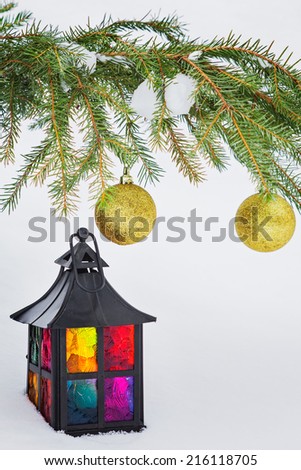Multicolored decorative lantern in the snow and fur-tree branch with Christmas balls