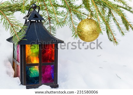 Multicolored decorative lantern in the snow and fur-tree branch with gold Christmas ball