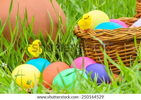 Painted Easter eggs and toy chickens on the background of a clay pitcher, wicker basket and green spring grass