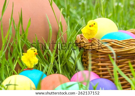 Painted Easter eggs and toy chickens on the background of a clay pitcher, wicker basket and green spring grass close up