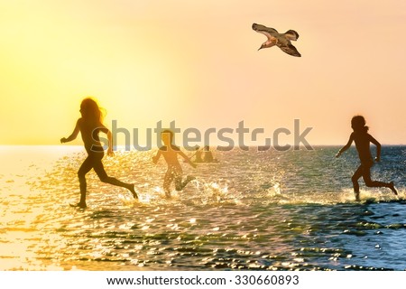Silhouettes of children running through the water at scenic sunset, backlit