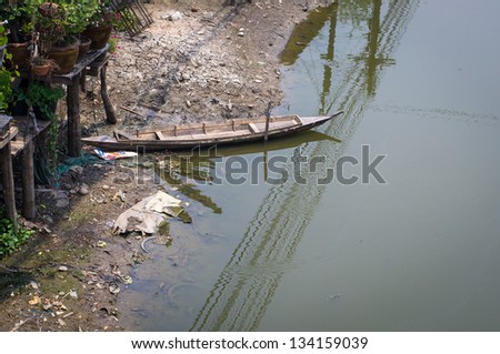 Wooden boat floating on river bank with electric wire reflection along the river