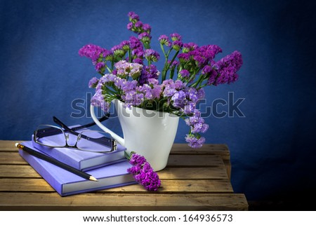 Glasses place on purple note books with flowers vase on wooden table
