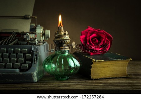 Ancient lantern on wooden table with red rose bud on old book and typewriter