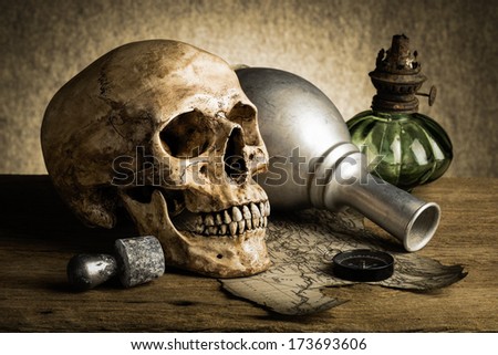 Still life, human skull with knife in the mouth beside old book, old compass on torn map and bottle of wine