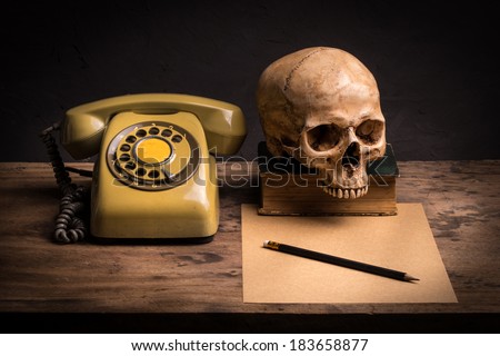 Still life with human skull, retro telephone and brown paper on wooden table