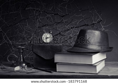 Still life with vintage leather hat on books, leather case brass candlestick and glasses