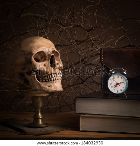 Still life with human skull on brass candlestick, leather case and clock on stack of books