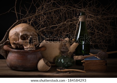 Still life human skull on clay pot with grunge lamp, old book, wooden spoon and green bottle