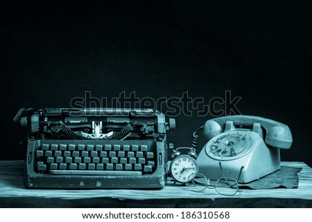 still life with old typewriter, telephone, alarm clock and glasses on wooden table