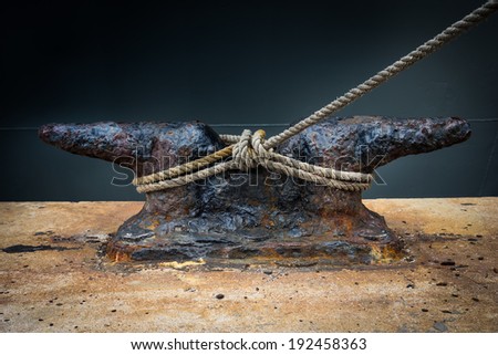 Rusty mooring rope with a knotted end tied around a cleat / Nautical mooring rope