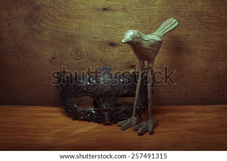 black fancy mask and bird candle stand on wooden background, still life