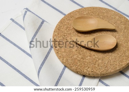 Wooden kitchen spoon on a cork plate and white napkin on a wooden counter