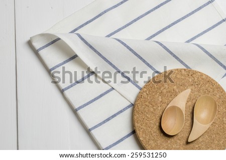 Wooden kitchen spoon on a cork plate and white napkin on a wooden counter