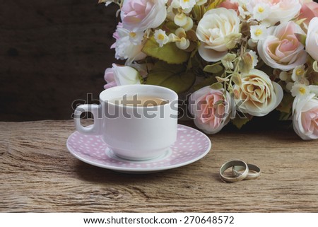 Cup of tea and couple of rings on wooden table with flowers, still life