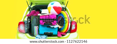Banner Summer Travel Time Overloaded Green Car Blue and Pink Trunks Straw Hat Slippers Rackets Towels Rug Yoga Two Suitcases Luggage Holiday Concept Adventure Trip. Isolated on Yellow Background