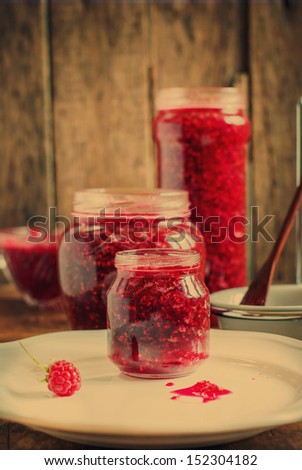 Jam from Raspberries in an open Jars on the wooden background, toned
