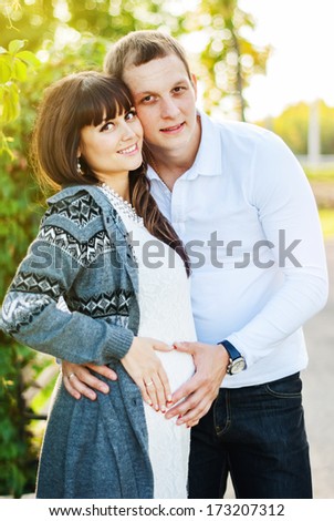 Man and Pregnant Woman making heart from hands on stomach in the Park, outdoor