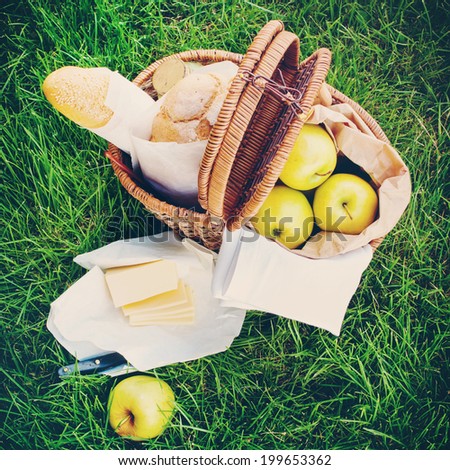 Fresh Bread, Apples, Cheese in a Wattled Basket on Green Grass, picnic