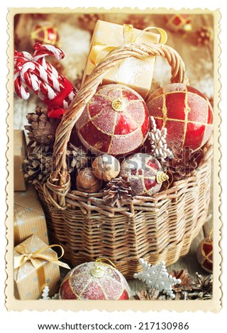 Vintage Card with Retro Frame. Gifts in Christmas Composition with Basket, Red balls, Pine cones, Sweet Candy toys, Pine cones, Boxes, Walnuts and snowflakes. Toned effect