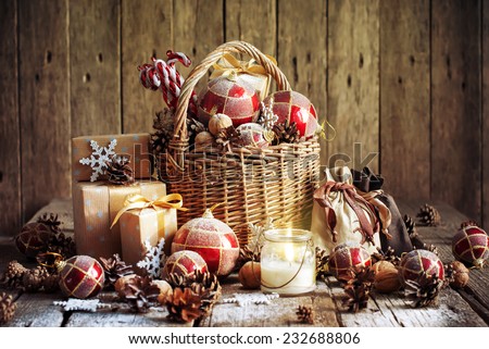 Christmas Basket with Vintage Gifts and Shining Candle. Red balls, Pine cones, Snowflakes, Boxes on Wooden Table. Warm Toned effect