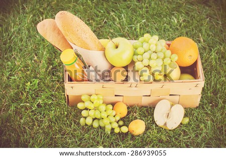 Picnic Wattled Basket with Fresh Food, Bread, Apples, Fruit on Green Grass. Horizontal image. Toned Image