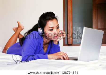 Young woman in a blue top and headphones using a laptop in bed