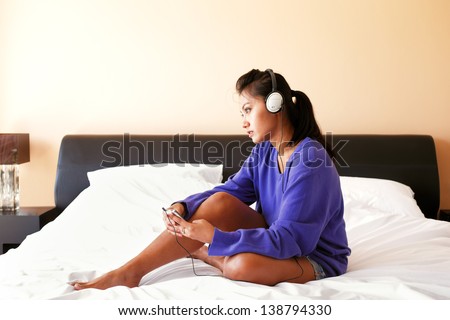 Young woman in a blue top and headphones listening to the music in bed