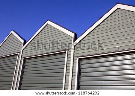 A row of uniform garages with roller doors on a blue sky background.