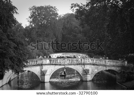 Black and white image of the Cam river in Cambridge with punt crossing under the bridge